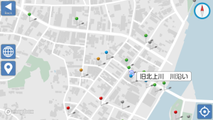 Interactive city map with colored pins marking locations, a left-side toolbar (Back, globe, and location icons), a blue compass on the right, and a river labeled 旧北上川沿い along the coast.